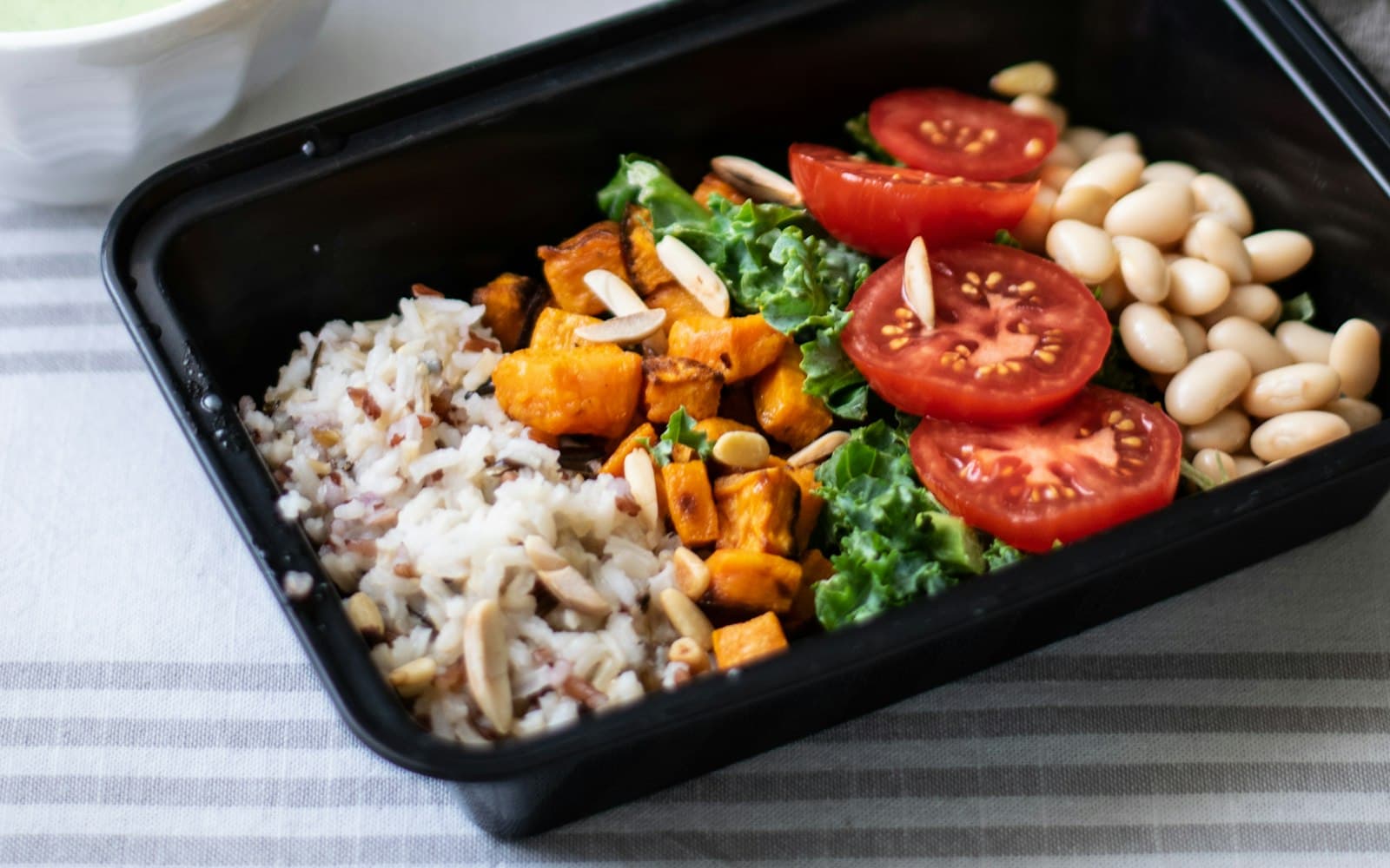 A meal-prep box of rice, roasted sweet potato, greens, tomatoes and white beans
